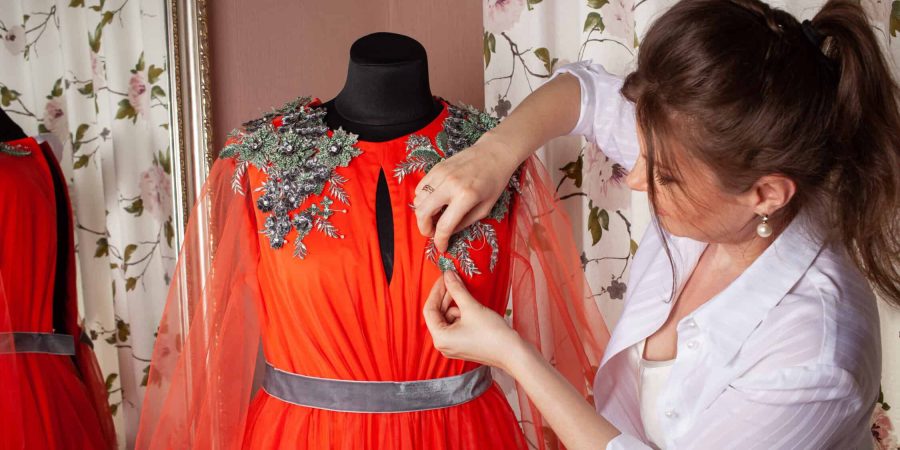 The seamstress sews lace and beads to the dress. A woman makes a dress with her own hands in a studio. Small business after coronavirus. A sewing studio.